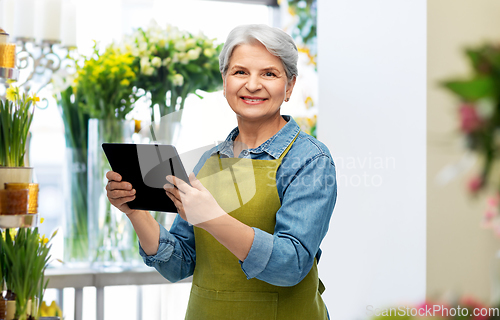 Image of happy senior woman in garden apron with tablet pc