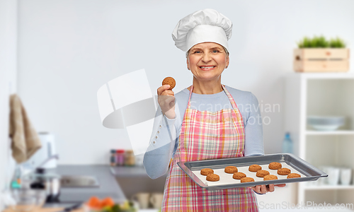 Image of senior woman in toque with cookies on baking pan