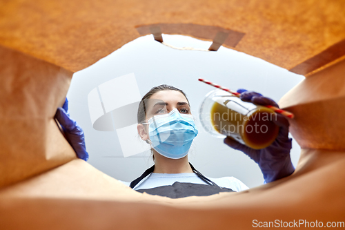 Image of saleswoman in gloves and mask packing food in bag