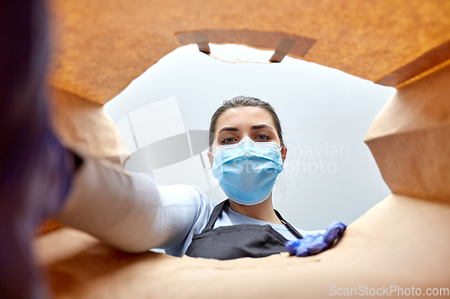 Image of saleswoman in gloves and mask packing food in bag