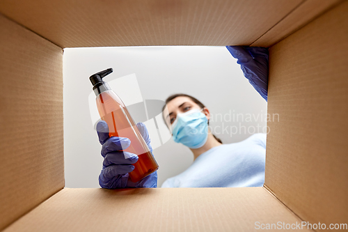 Image of woman in mask unpacking parcel box with cosmetics