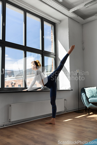 Image of woman doing yoga exercise at window sill at studio