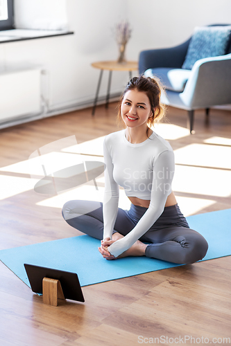 Image of young woman with tablet pc doing yoga at home