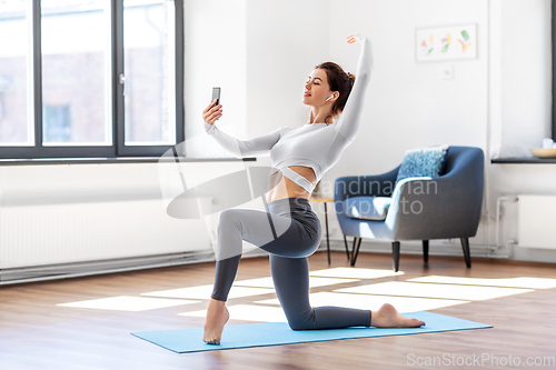 Image of young woman with smartphone doing yoga at home