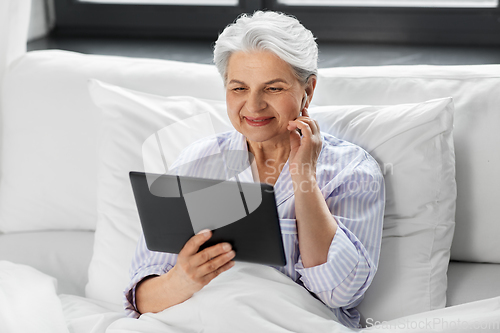 Image of senior woman with tablet pc and earphones in bed