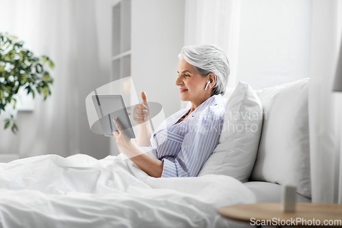 Image of old woman with tablet pc having video call in bed