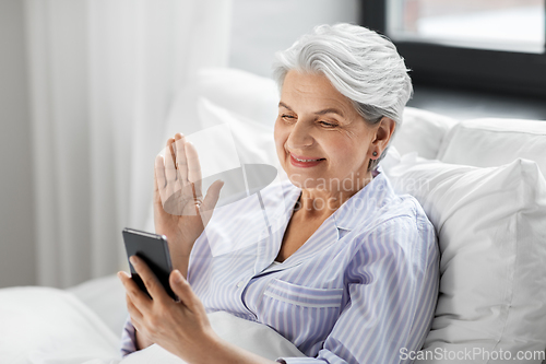 Image of senior woman with phone having video call in bed