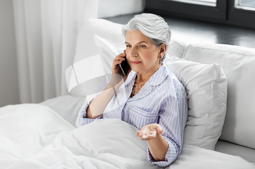 Image of senior woman calling on smartphone in bed at home