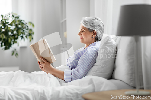 Image of senior woman reading book in bed at home bedroom