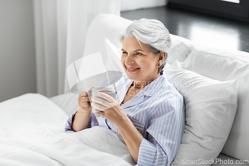 Image of old woman with cup of coffee in bed at home