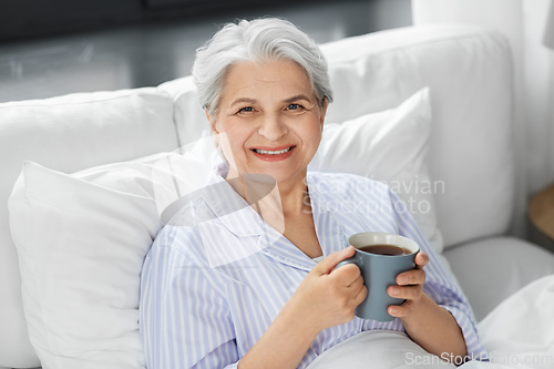 Image of old woman with cup of coffee in bed at home