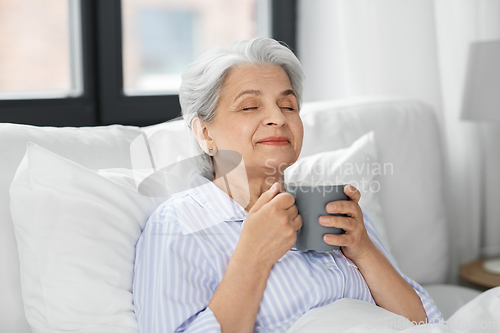 Image of old woman with cup of coffee in bed at home