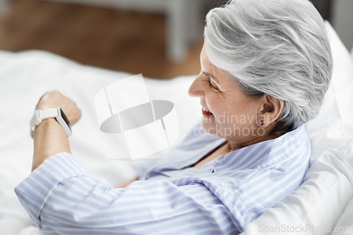 Image of happy senior woman sitting in bed at home bedroom