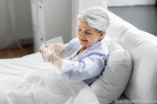 Image of happy senior woman sitting in bed at home bedroom