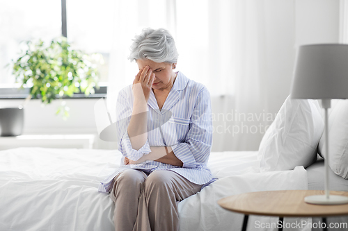 Image of senior woman with headache sitting on bed at home