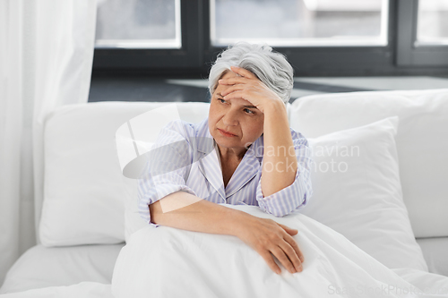 Image of senior woman with headache sitting in bed at home