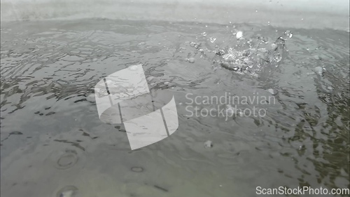 Image of Rain water drops falling into big puddle on asphalt, flooding the street. Road floods due to the heavy rain in wet season. Raindrops falling down onto submerged road.