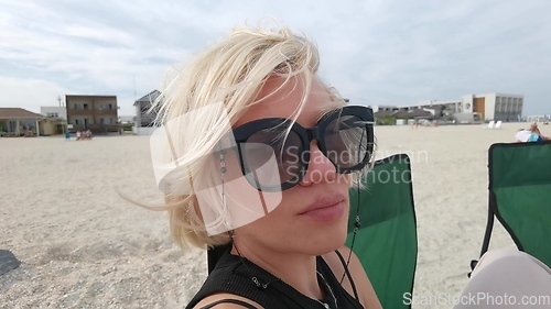 Image of Slow motion portrait face of beautiful young woman with short blonde hair looking at camera sitting on sea beach