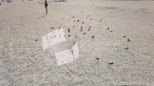 Image of Kid girl on a beach play with birds flying near waterline of sea.