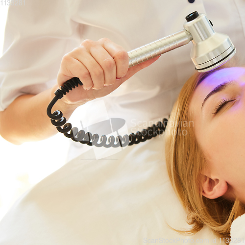 Image of Young healthy woman with good skin doing cosmetic procedures in spa clinic. Light treatment.