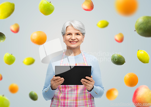 Image of smiling senior woman in apron with tablet computer