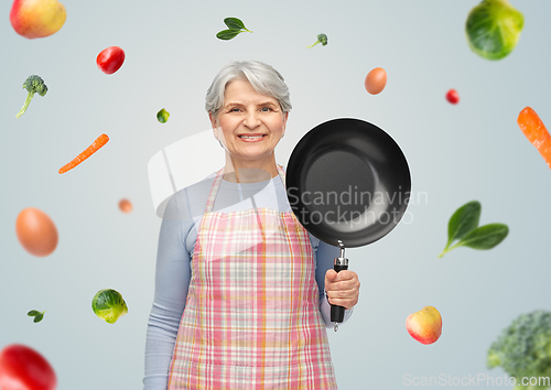 Image of smiling senior woman in apron with frying pan