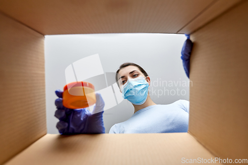 Image of woman in mask unpacking parcel box with cosmetics