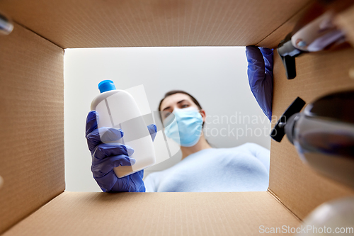 Image of woman in mask unpacking parcel box with cosmetics