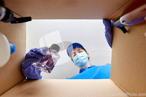 Image of woman in mask packing parcel box with cosmetics