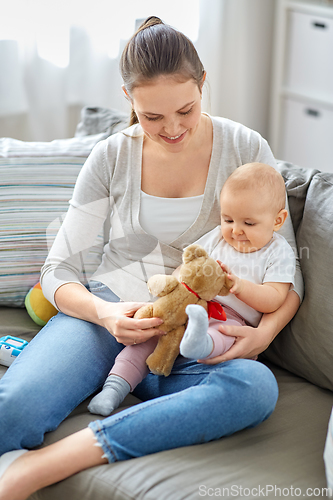 Image of mother with baby playing with teddy bear at home