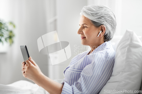 Image of senior woman with tablet pc and earphones in bed