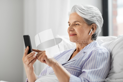 Image of senior woman with smartphone and earphones in bed