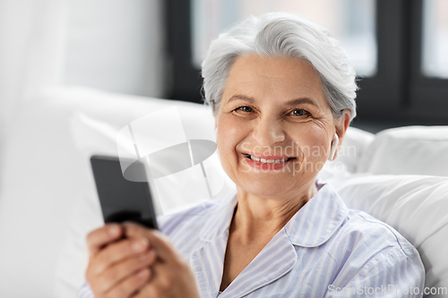 Image of senior woman with smartphone and earphones in bed