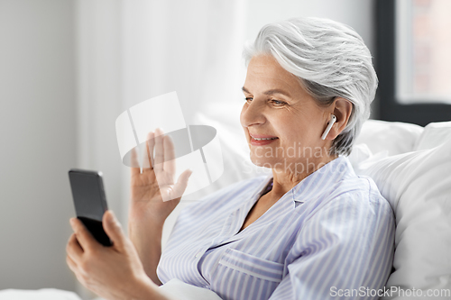 Image of senior woman with phone having video call in bed