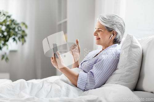 Image of senior woman with phone having video call in bed