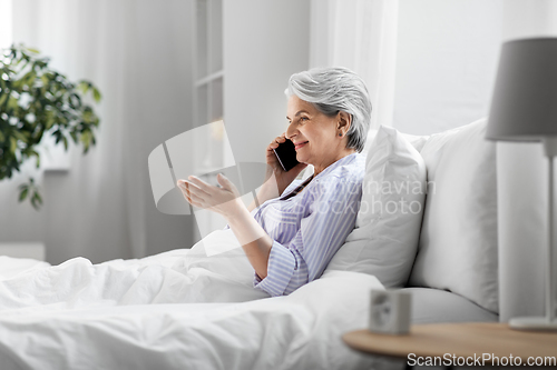 Image of senior woman calling on smartphone in bed at home