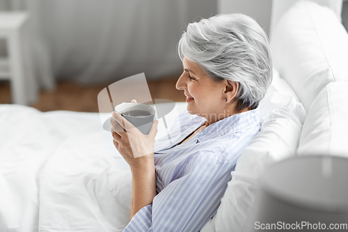 Image of old woman with cup of coffee in bed at home