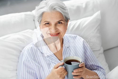 Image of old woman with cup of coffee in bed at home