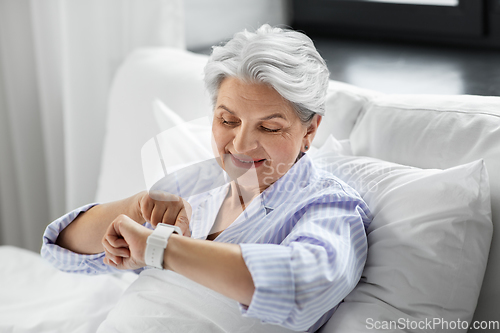 Image of happy senior woman sitting in bed at home bedroom