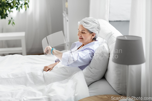 Image of happy old woman with health tracker sitting in bed