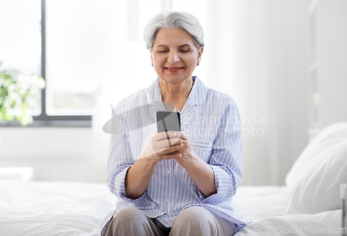 Image of happy senior woman with smartphone on bed at home