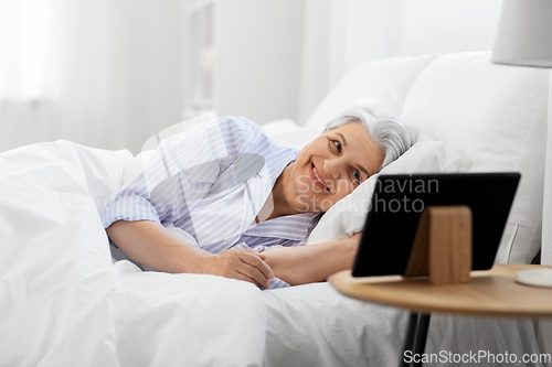 Image of happy senior woman with tablet pc in bed at home