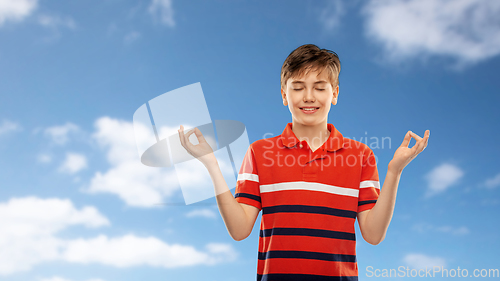 Image of happy smiling meditating boy over blue sky