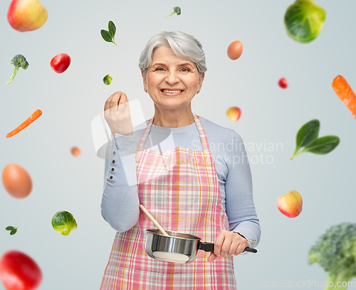 Image of senior woman in apron with pot cooking food