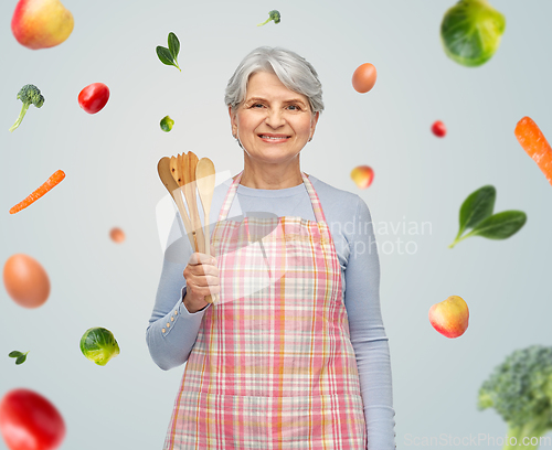 Image of smiling senior woman in apron with wooden spoons