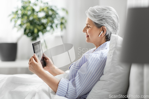 Image of senior woman with tablet pc and earphones in bed