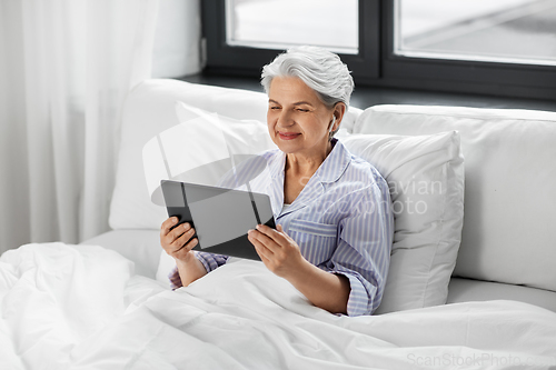 Image of senior woman with tablet pc and earphones in bed