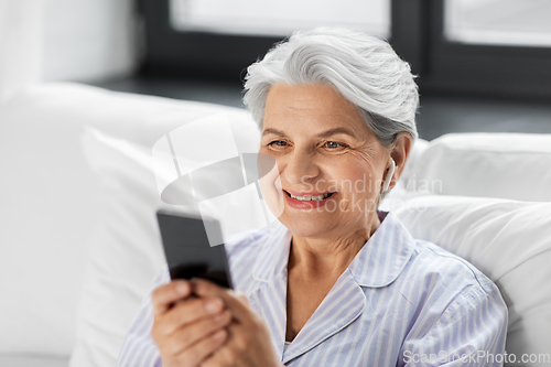 Image of senior woman with smartphone and earphones in bed