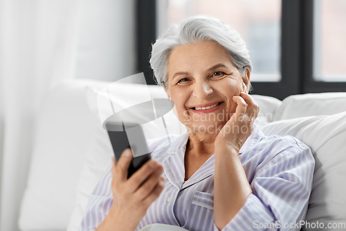 Image of senior woman with smartphone and earphones in bed