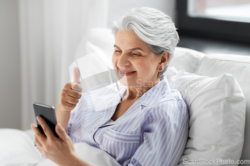 Image of senior woman with phone having video call in bed